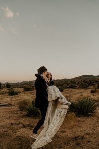 joshua-tree-wedding-bride-swept-up-by-her-groom-wearing-backless-bohemian-lace-dress-with-pink-converse