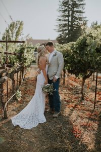 sexy-bride-with-her-groom-in-the-vineyards-in-Californai-wearingh-penelope-lace-dress-with-front-slits