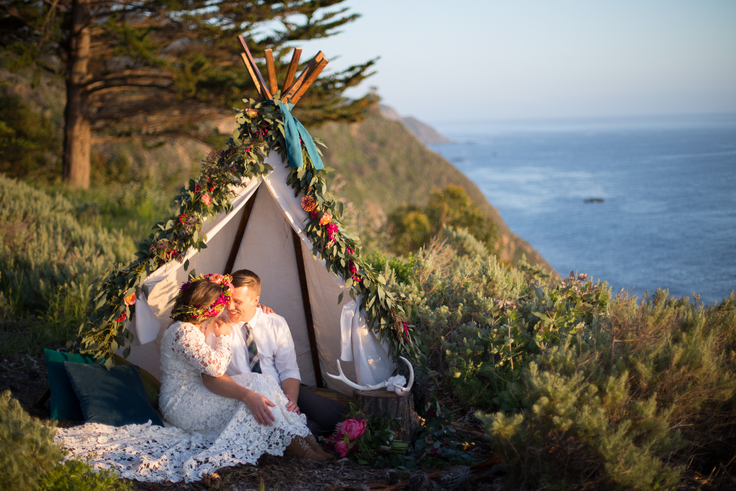 tropical-bohemian-wedding-captured-in-Big-Sur-lovers-cozy-up-in-a-teepee-bride-wearing-a-aimple-long-sleeve-wedding-dress