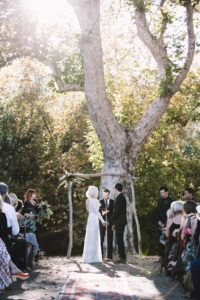 bride-wearing-lisa-backless-dress-with-her-husband-under-a-tree-arched-altar-saying-their-I-dos