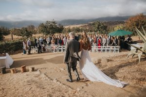 a-laidback-bride-faces-her-wedding-guests-as-she-walks-with-her-father-at-her-California-ranch-wedding