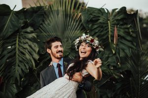 happy-bride-being-carried-by-her-new-husband-she-wears-a-tropical-flower-crown-and-a-simpe-lace-dress