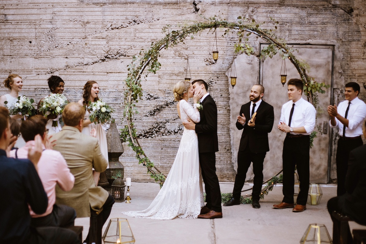 stunning-bride-and-groom-kisses-at-their-bohemian-alter-her-in-a-long-sleeved-backless-lace-wedding-dress