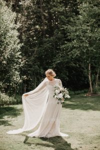 bohemian-bride-wearing-dreamy-simple-long-veil-with-a-subtle-green-white-bouquet-in-a-whimsical-lace-flowy-wedding-dress-with-nature-as-the-perfect-backdrop
