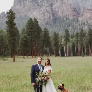 Real bride in an open field wearing an off the shoulder lace wedding dress with her husband and dog
