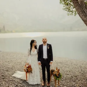 California Bridal Showroom | Real bride wearing a flowy lace wedding dress next to a lake wither new husband and dog by her side